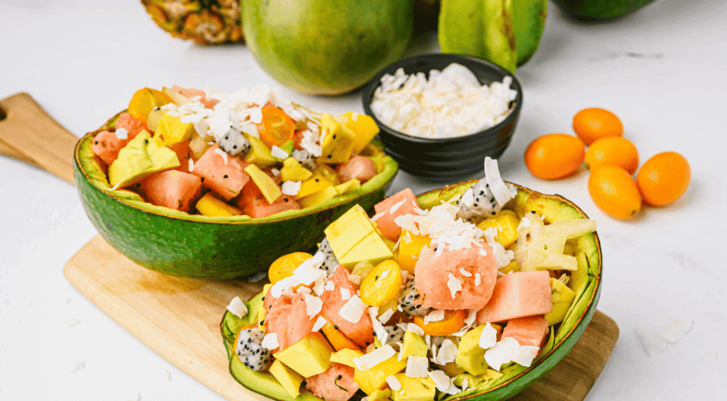 Overview of Tropical Fruit salad in tropical avocados on a cutting board with tropical fruits in the background