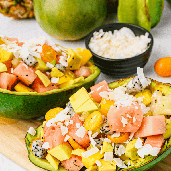 Overview of Tropical Fruit salad in tropical avocados on a cutting board with tropical fruits in the background