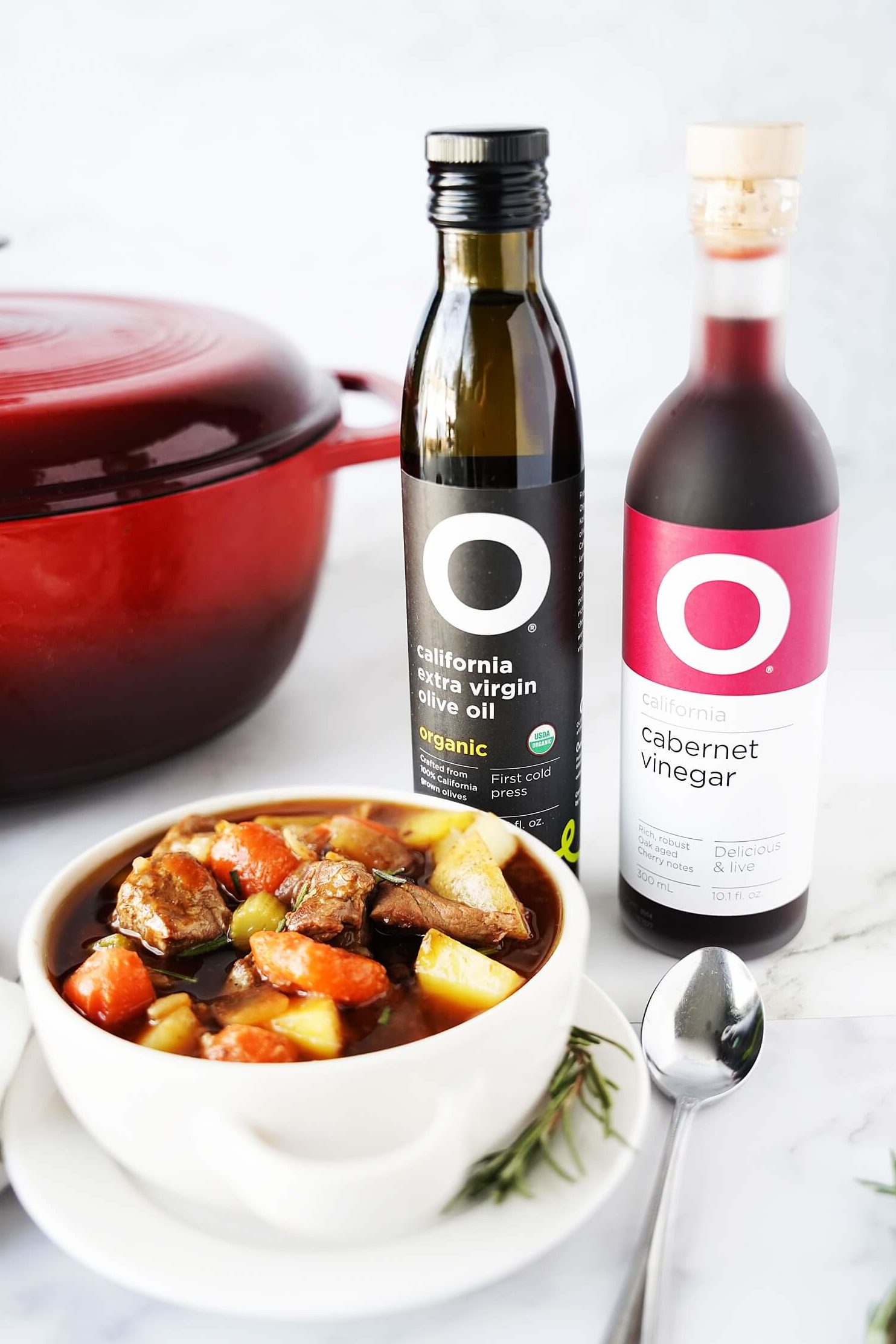 Beef Stew in bowl with pot in background with O Olive Oil bottles