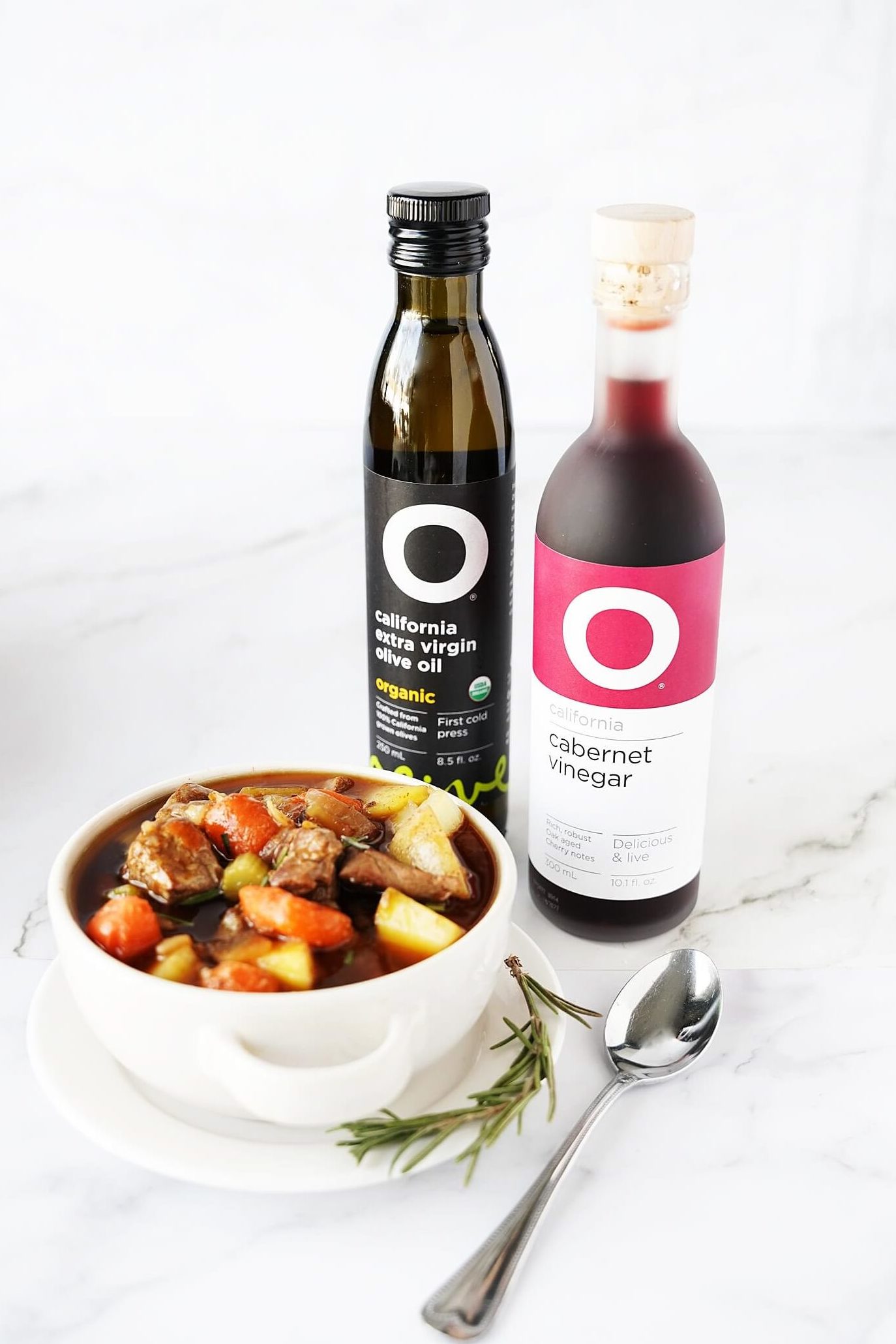 vertical image of beef stew in bowl with O Olive Oil & Vinegar bottles