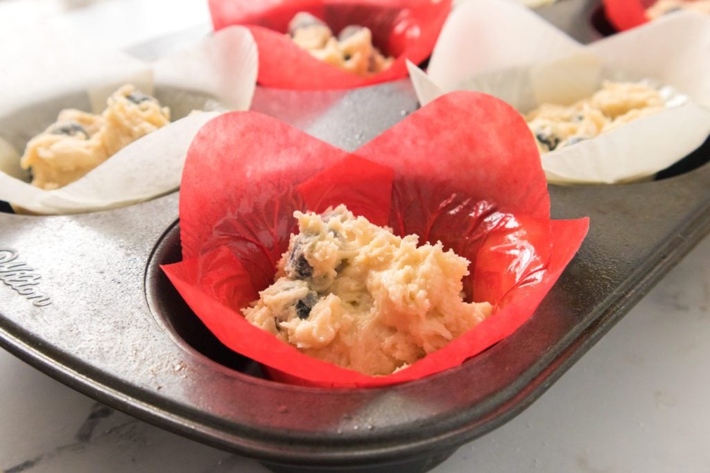 blueberry muffin batter in muffin tin with red and white muffin liners