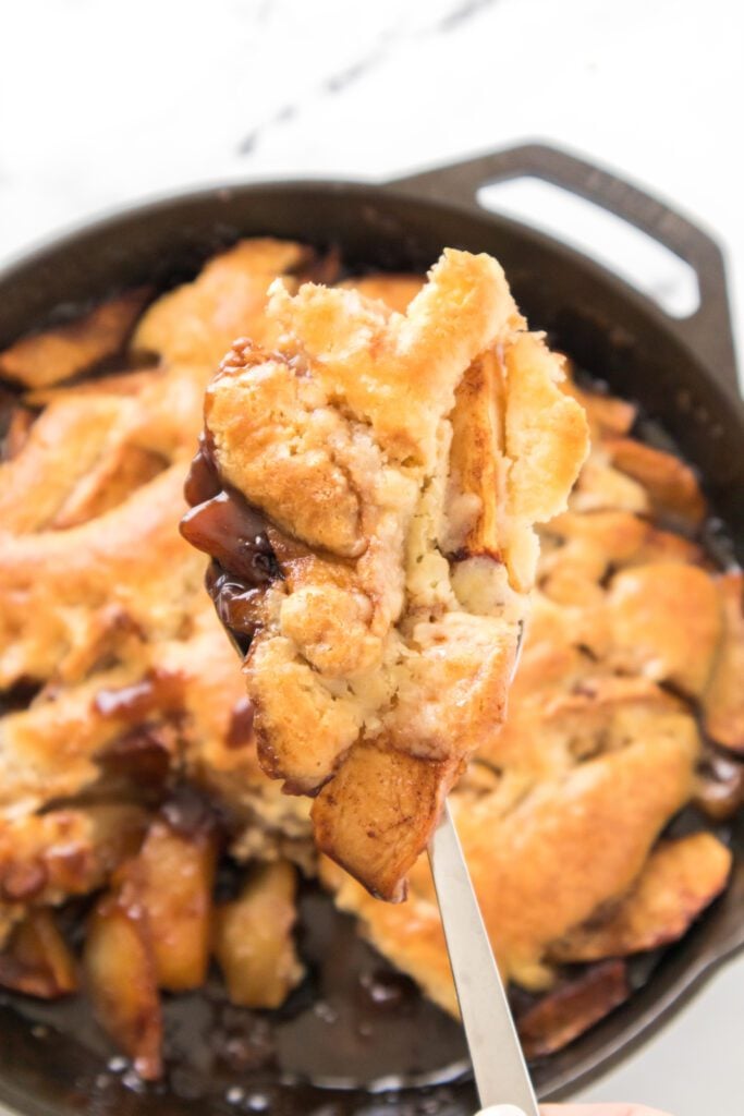 spoonful of apple cobbler baked in a cast iron skillet in the background