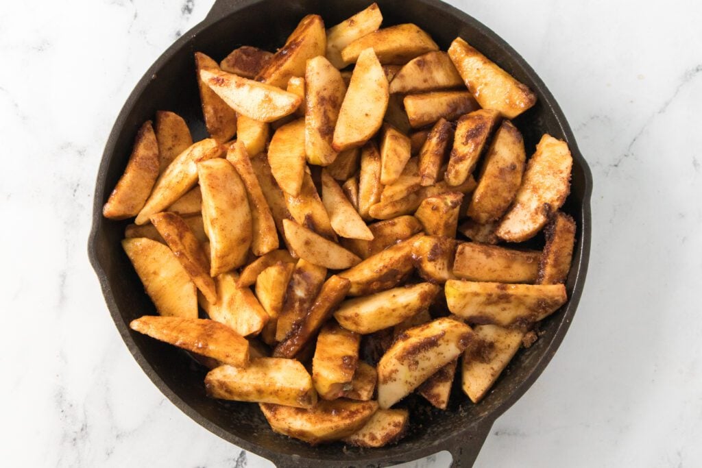 apple slices tossed with spices and brown sugar in a cast iron skillet