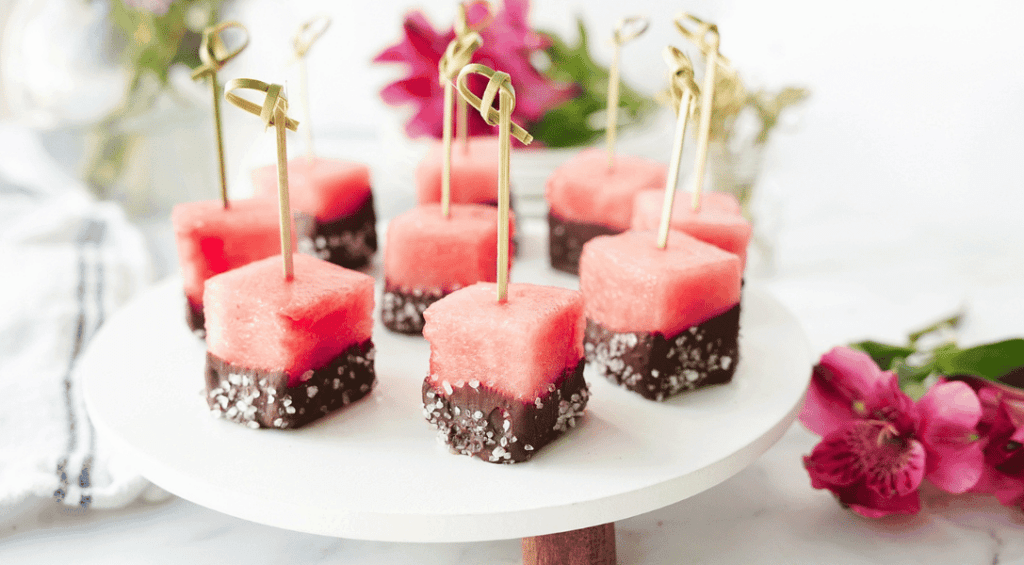 Chocolate covered watermelon bites on white stand with flowers in the background