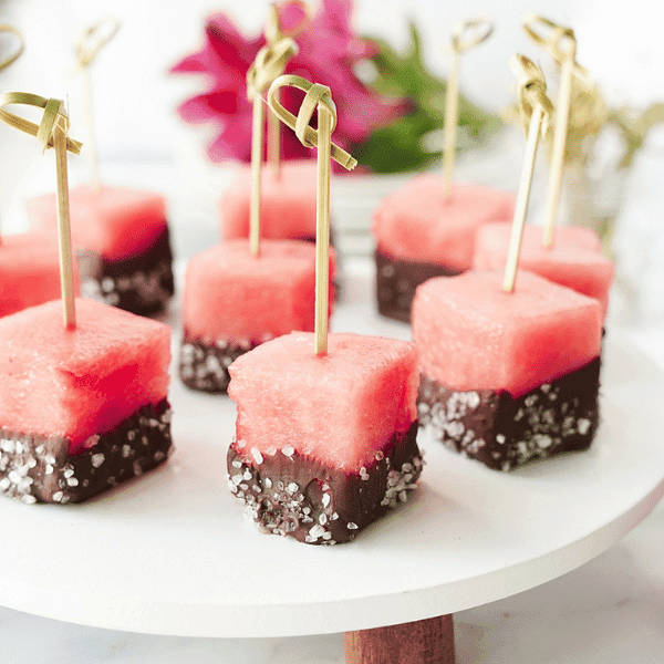 Chocolate covered watermelon bites on white stand with flowers in the background