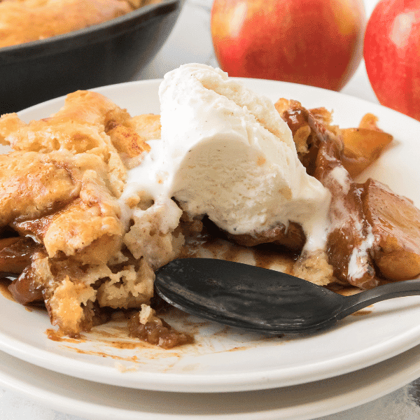 Piece of apple cobbler on plate with ice cream on top and spoon