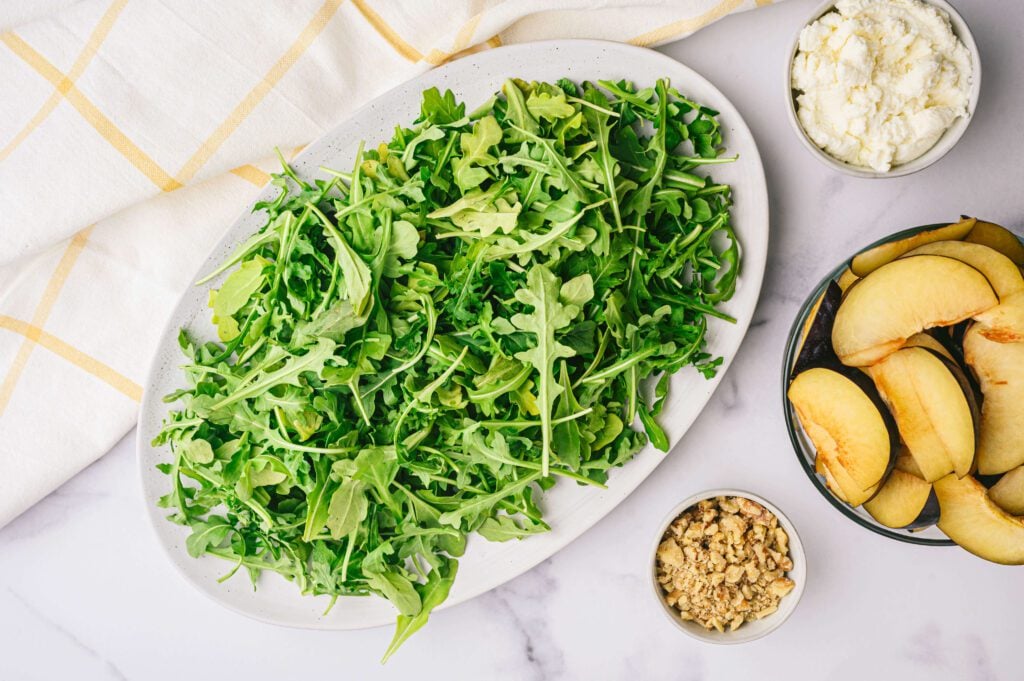 Plate of arugula with ricotta cheese, walnuts and sliced plums in small bowls