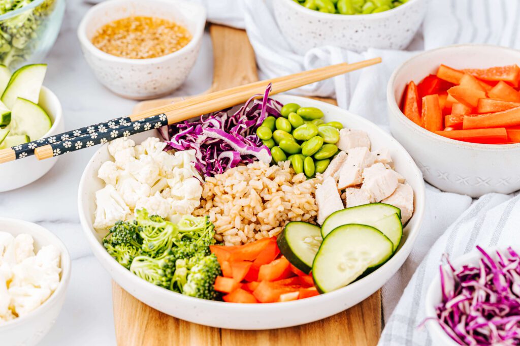 Asian Grain bowl in white dish with chopsticks surrounded by veggies