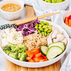 Asian Grain bowl in white dish with chopsticks surrounded by veggies