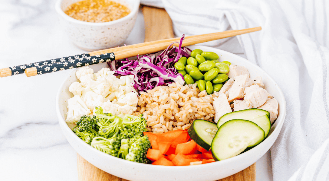 Asian Grain bowl with veggies in a white bowl with chopsticks and sauce in background