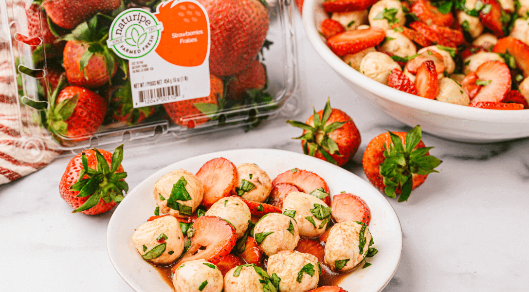 Strawberry Caprese Salad in a bowl with Naturipe strawberry in the background