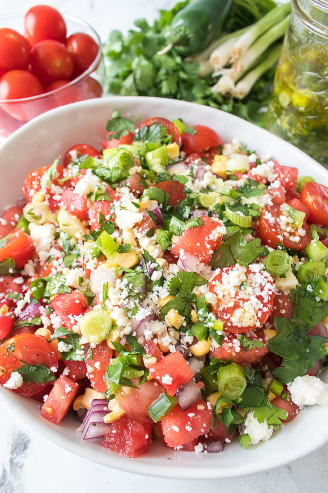 close up of tomato and watermelon salad with veggies in the background