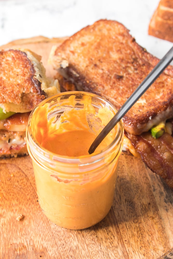 vertical shot of tomato aioli in mason jar with bacon avocado grilled cheese in background