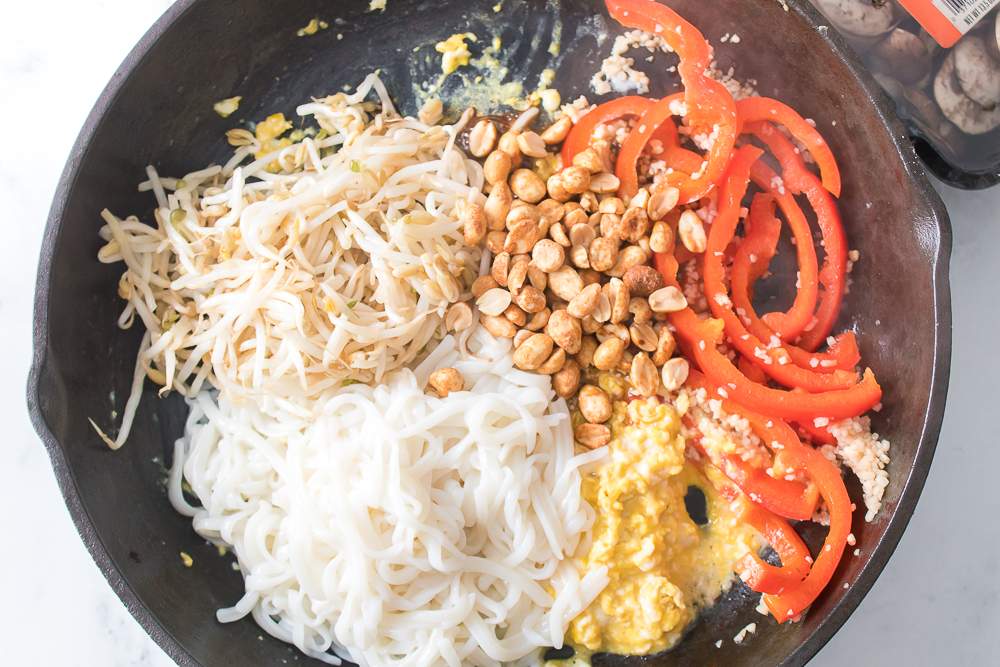 overhead shot of bean sprouts, rice nooodles, scrambled eggs, bell pepper, garlic and peanuts in cast iron skillet