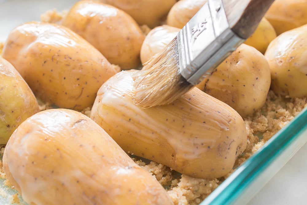 potatoes in casserole dish brushing on melted butter