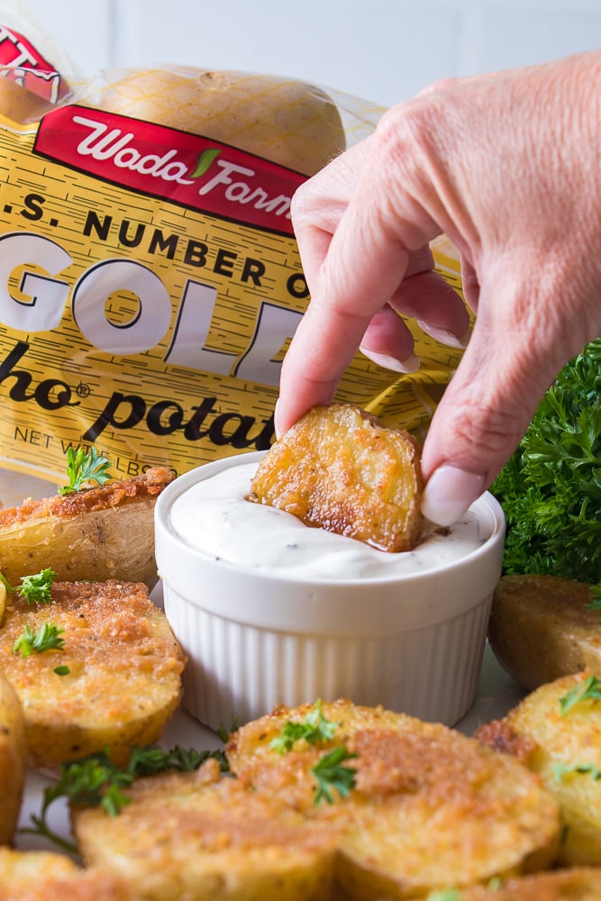 vertical image of a hand dunking oven roasted potato into ranch dressing