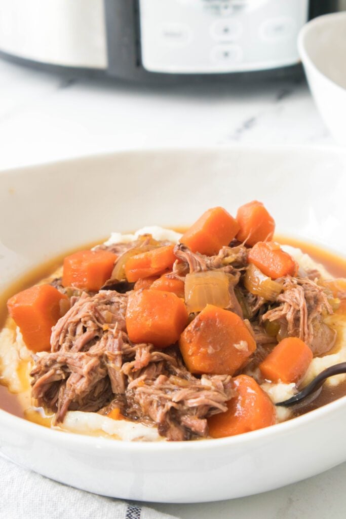 close up of pot roast over mashed potatoes in white bowl with spoon
