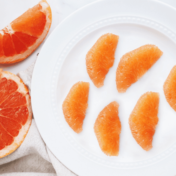 Grapefruit segments on plate with slice and halved grapefruit in back