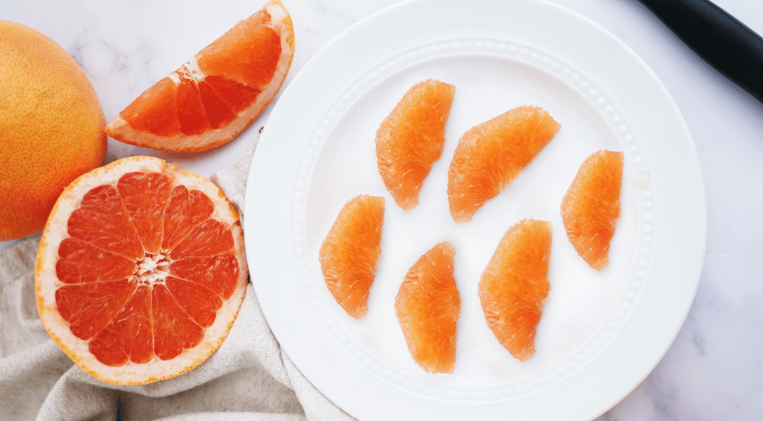 Grapefruit segments on plate with slice and halved grapefruit in back