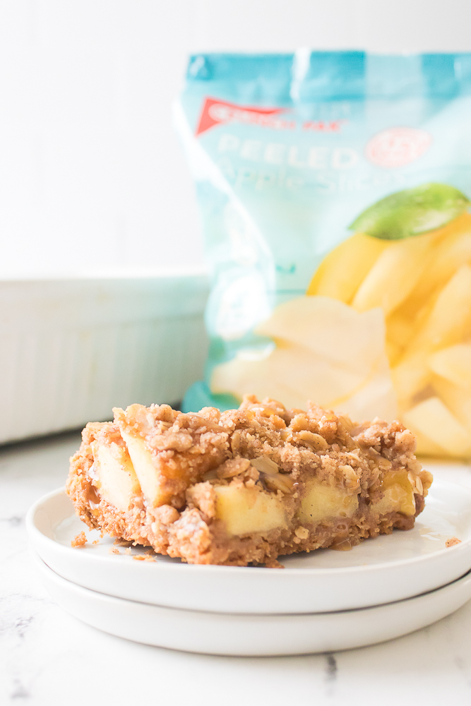 apple crisp bar on white plate with bag of Crunch Pak apples in background