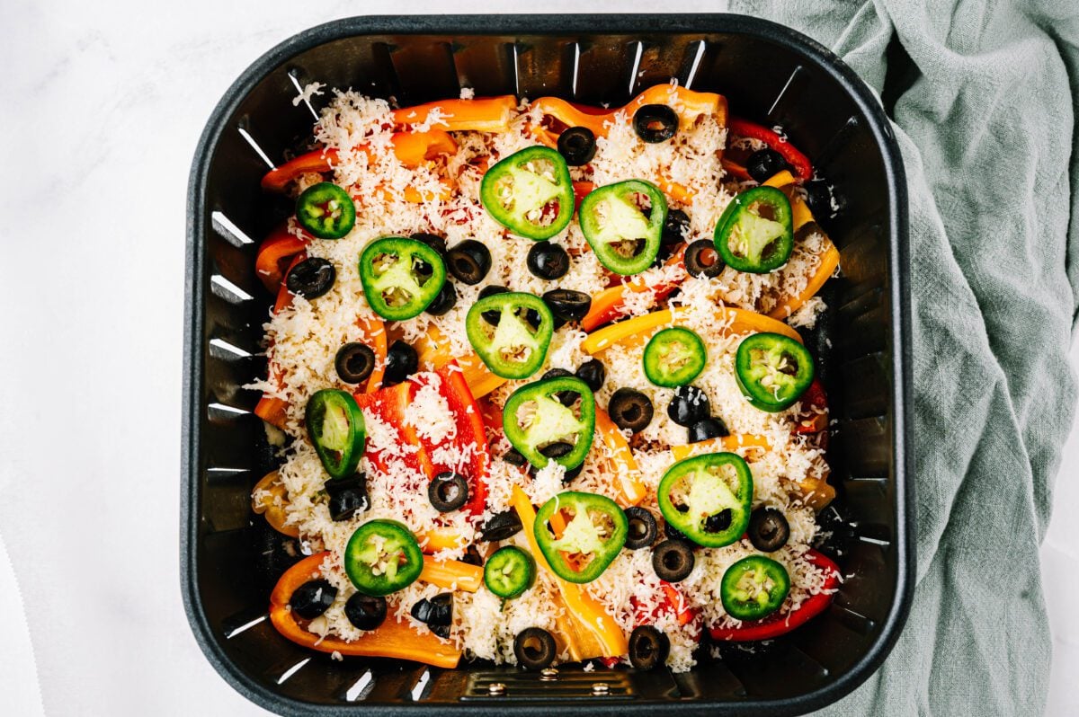bell peppers covered with shredded cheese, olive and jalapeño slices in air fryer basket