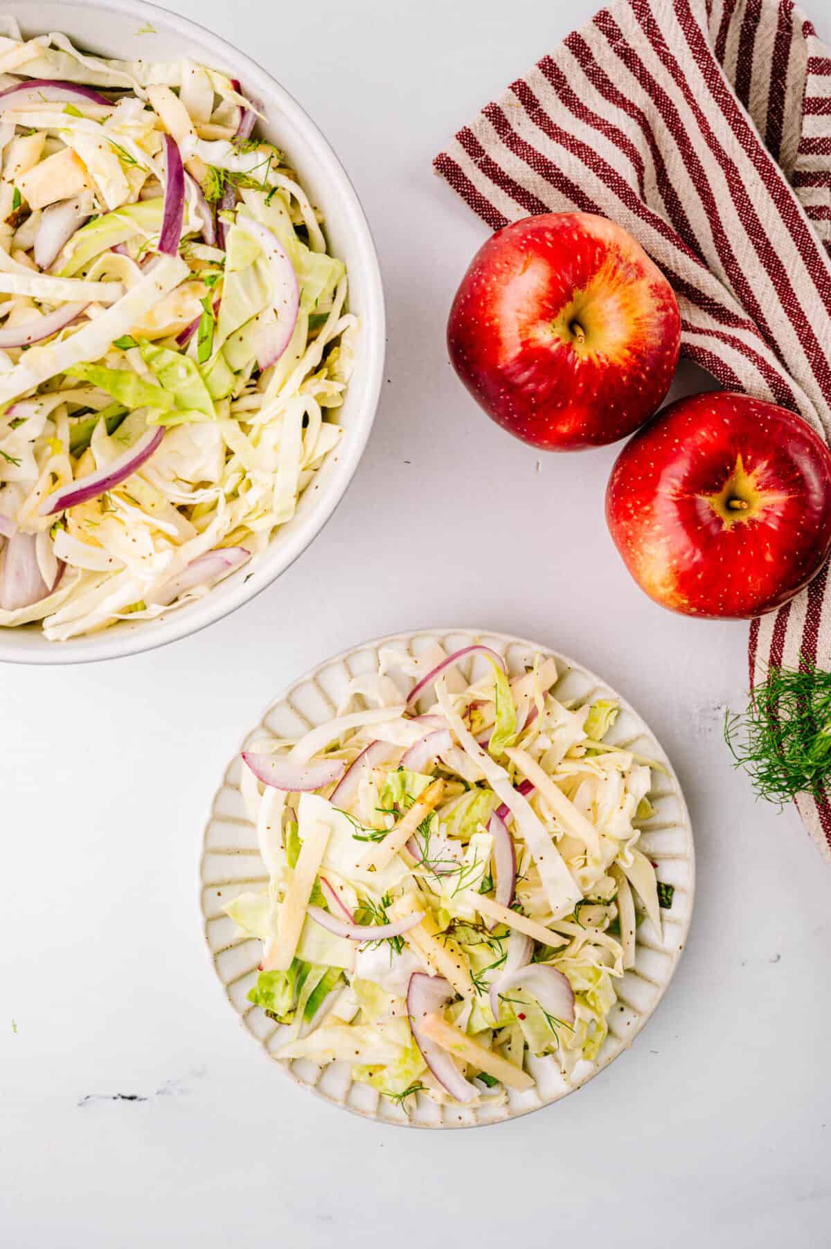 overhead shot of fennel apple salad on plate with bowl and two red apples