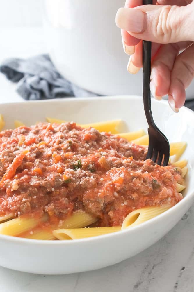 bowl with bolognese sauce over pasta with hand taking a bite with fork