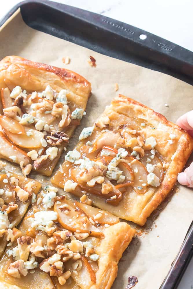 hand reaching for pear and blue cheese tart on baking sheet