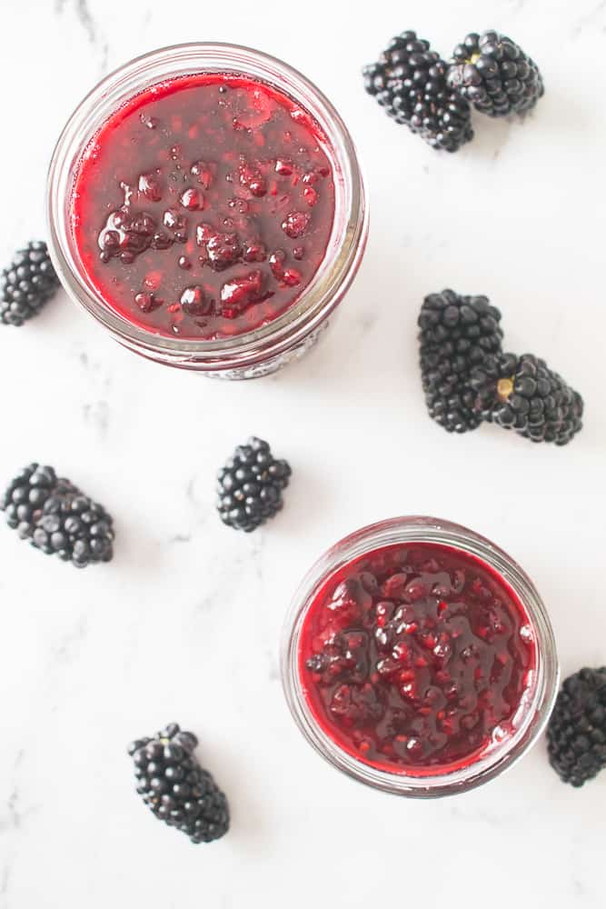 overhead shot of a mason jar and jelly jar filled with blackberry jam and blackberries scattered