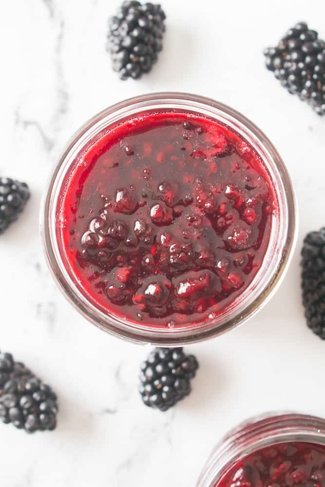 close up overhead shot of blackberry jam in mason jar with blackberries scattered