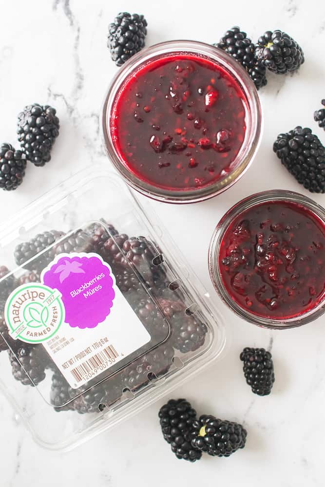 overhead shot of blackberry jam in mason jars with blackberries scattered