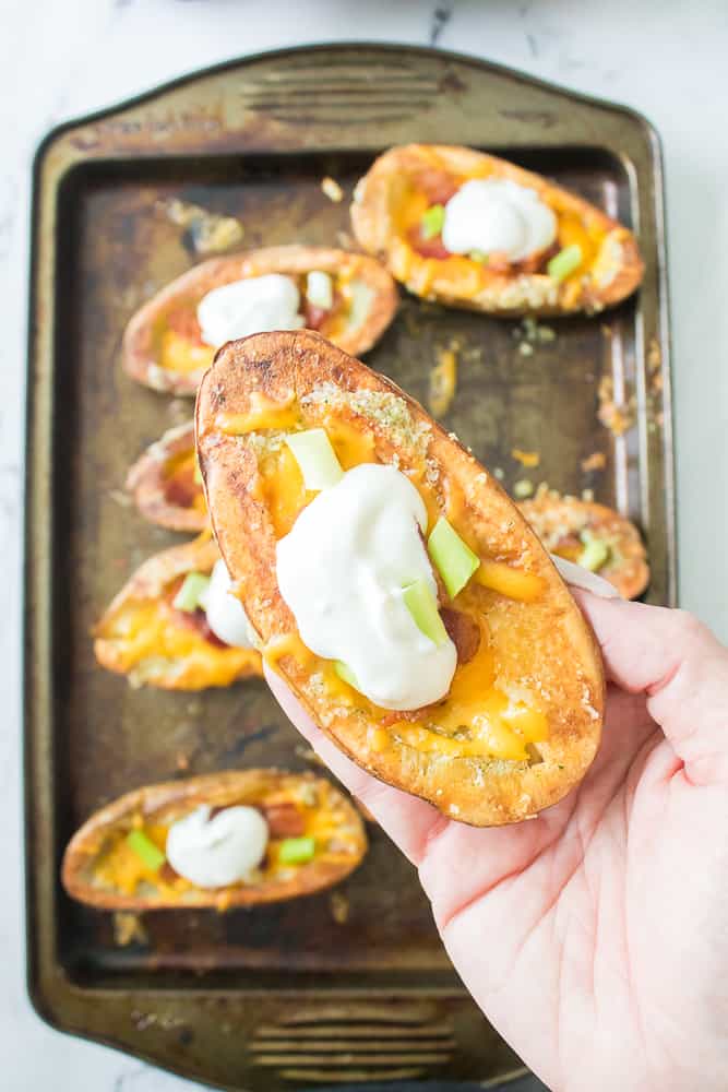 vertical image of a hand holding a loaded potato skin topped with sour cream 