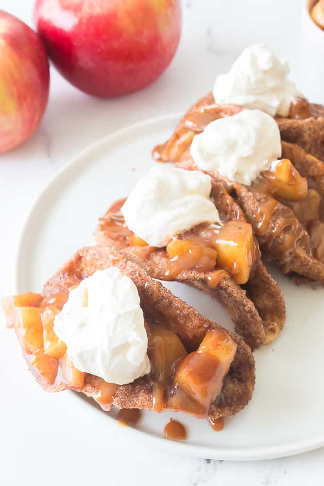 apple pie tacos on white plate with caramel sauce and cool whip