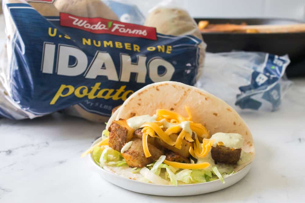 head on shot of potato taco with bag of wada farms idaho potatoes in the background