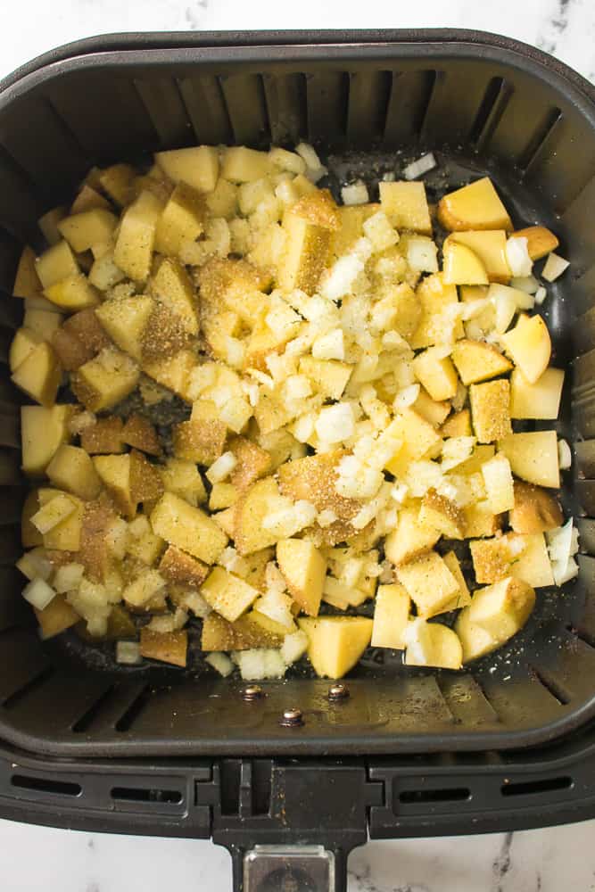 potatoes and onions in air fryer basket with seasonings