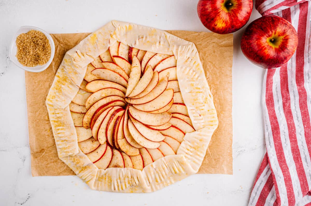 apples in a circle pattern in pie crust that has been crimped with a fork and coated in butter and sugar