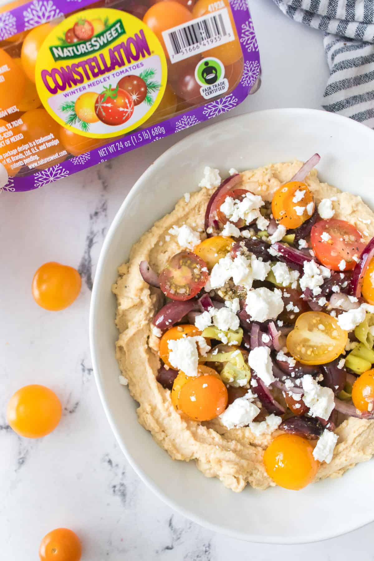 vertical overhead close up shot of loaded greek hummus with cherry tomatoes, red onion and feta