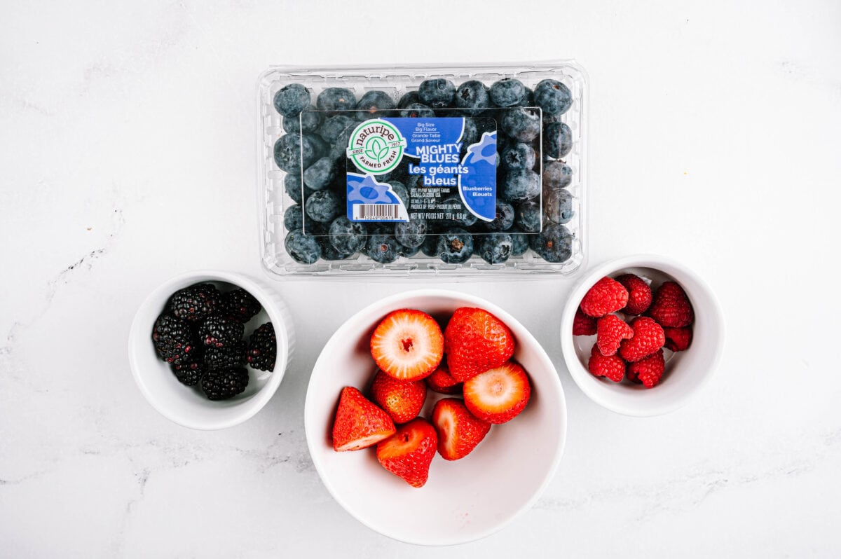 overhead shot of naturipe mighty blue blueberries in packaging with blackberries, strawberries and raspberries in white bowls