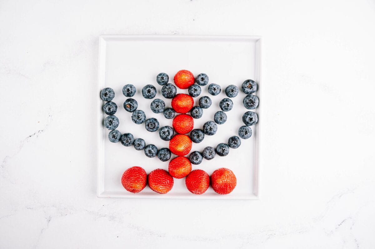 strawberries and blueberries on a plate layed out to look like a menorah