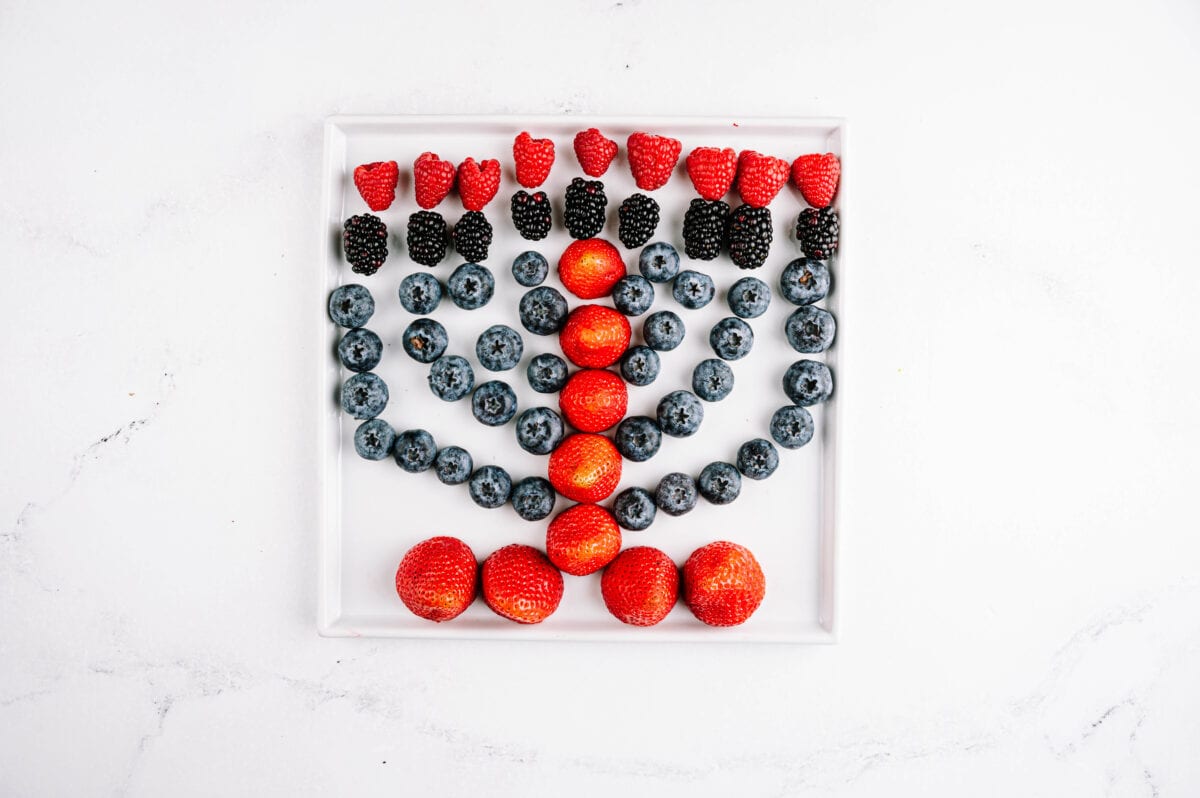 strawberries, blackberries and blueberries on a plate laid out to look like a menorah with raspberries as the flame