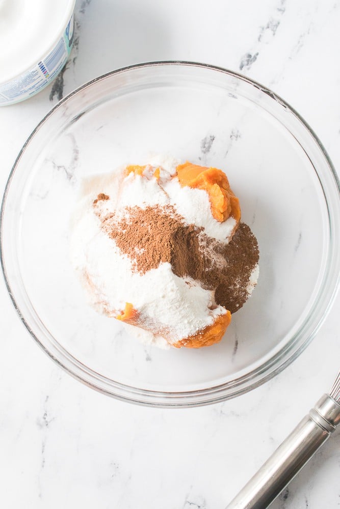 over head shot of canned pumpkin, vanilla pudding and pumpkin pie spice in glass bowl