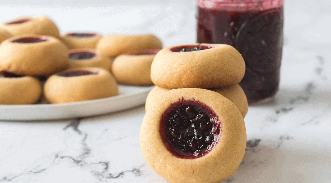 Stack of Thumbprint cookies with plate of cookies and blackberry jam in background