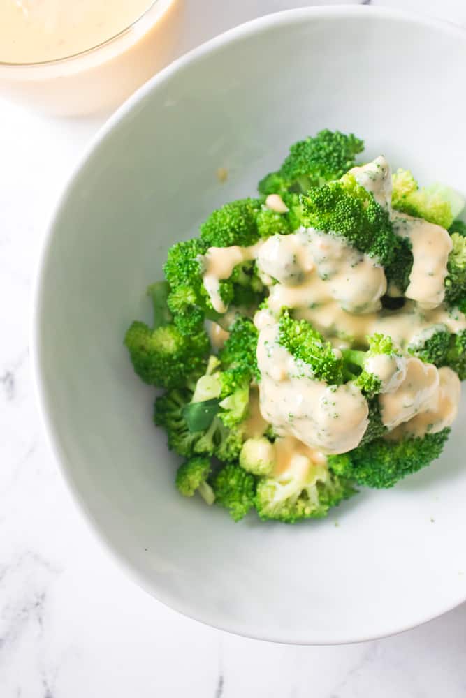 overhead shot of broccoli in white bowl topped with creamy cheese sauce