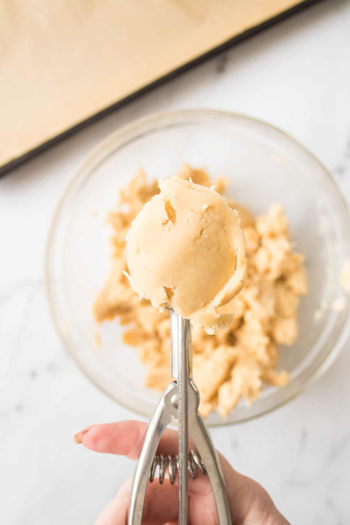 thumbprint cookie dough in cookie scoop over glass bowl with cookie dough