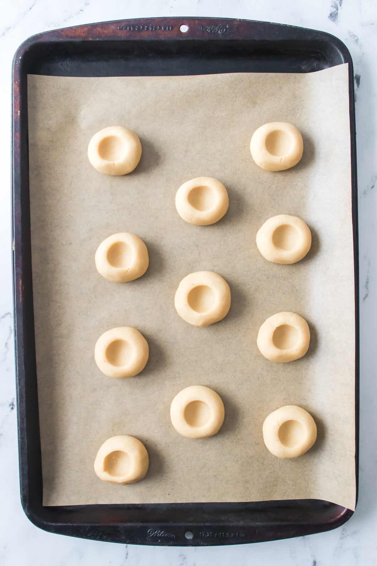 thumbprint cookies unbaked on baking sheet with indent for jam