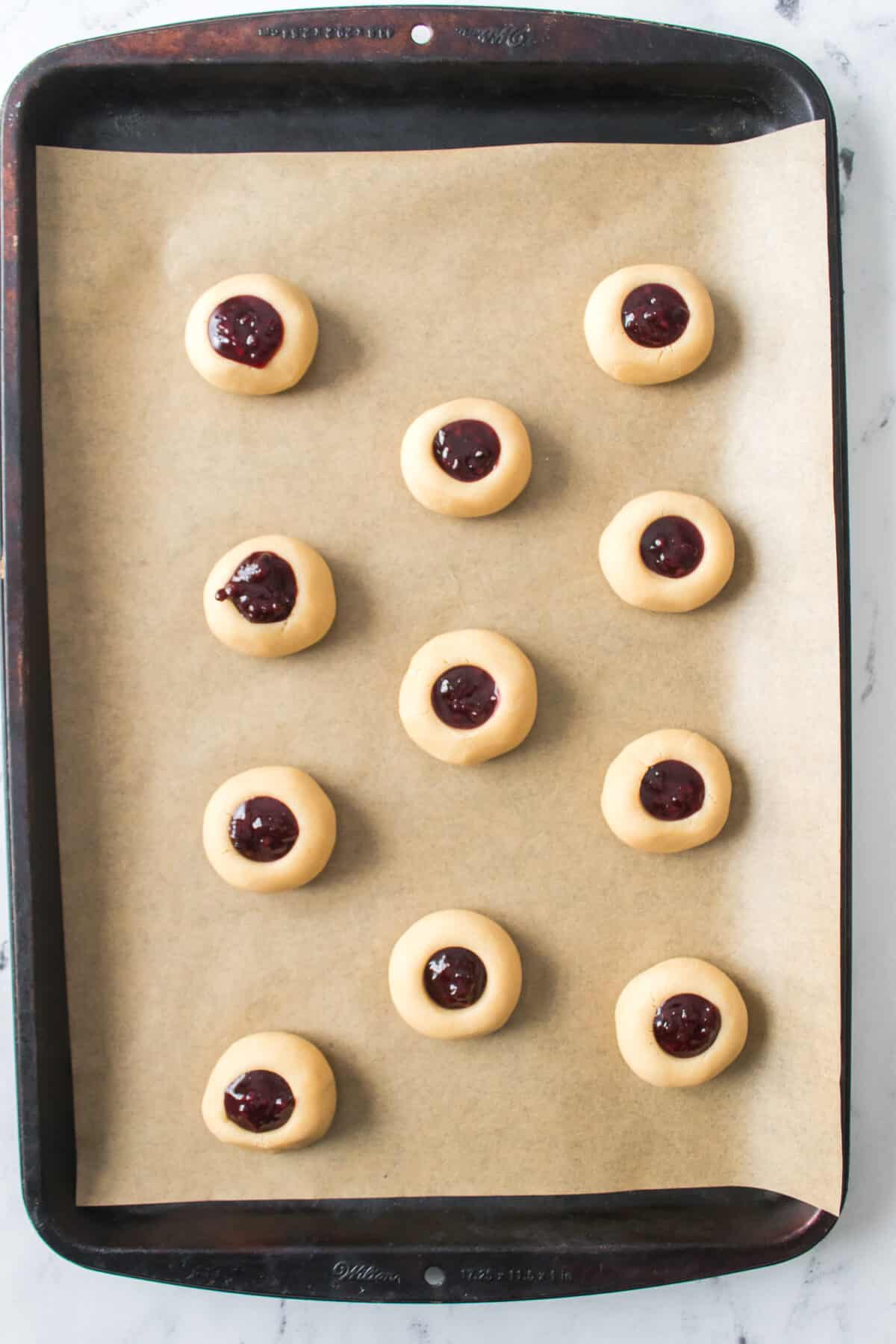 thumbprint cookies with blackberry jam on baking sheet before baking