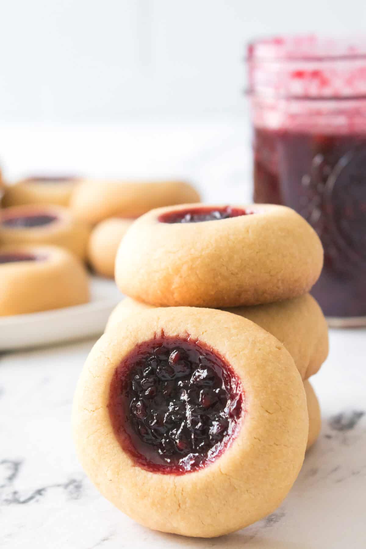 vertical shot of thumbprint cookies with blackberry jam with cookies on plate and jar of jam in background