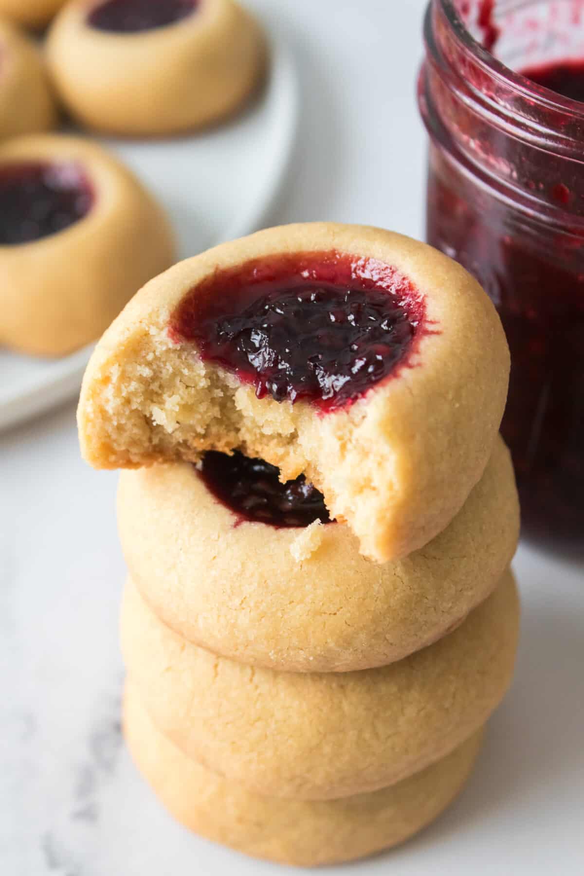 vertical close up shot of bite taken out of blackberry jam filled thumbprint cookie