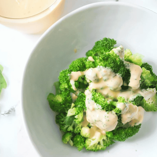 Bowl of broccoli with cheese sauce with cheese sauce in background
