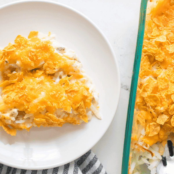 Funeral potatoes on a white plate next to glass dish serving funeral potatoes